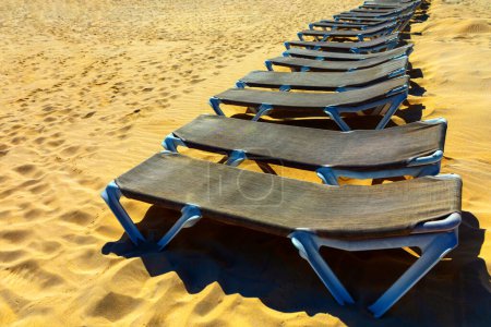 Sun loungers in a row on the sandy beach. Beach chairs stretches across the sandy shore. Place for summer sunbathing 