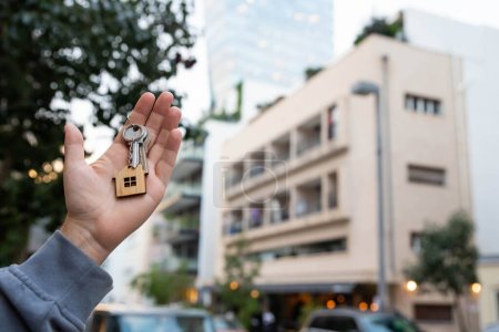 Photo for Buying a house, building repair and mortgage concept. Estimation real estate property with loan money and banking. Keys with toy home keychain charm in hand on city building background. - Royalty Free Image