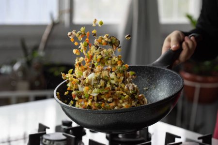 Foto de Chef cocinar asados verduras con mariscos en sartén wok en la estufa de gas. Levitación de alimentos vegetales voladores en movimiento, hábilmente sacudido por la mano del chef. Experiencia culinaria creativa en el aire. - Imagen libre de derechos