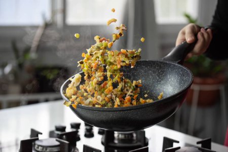 Téléchargez les photos : Chef cuisinier rôtit les légumes avec des fruits de mer dans wok casserole sur cuisinière à gaz. Légumes volants lévitation alimentaire en mouvement, habilement jeté par la main du chef. Expertise culinaire créative aéroportée. - en image libre de droit