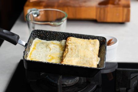 Foto de Chef man hands cooking Tamagoyaki or Tamago traditional Japanese Rolled Omelette recipe, made by rolling several layers of cooked scrambled whisking eggs in pan into a rectangular omelet. - Imagen libre de derechos