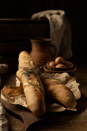 Photo for Homemade baguette french bread with parchment paper on wood table. Bread at wooden tabletop as baking concept - Royalty Free Image