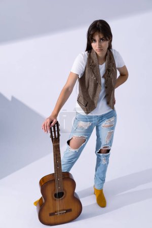 Photo for Young woman holdilng acoustic guitar. Musician in life style standing with classic guitar - Royalty Free Image