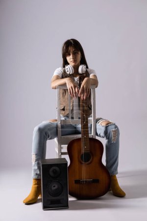 Photo for Young woman holdilng acoustic guitar sitting on a chair. Musician in studio with classic guitar - Royalty Free Image