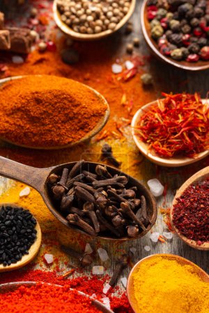 Photo for Clove pepper in spoon and mix of variety spices on table background. Dried spice and seeds as ingredients at kitchen table closeup - Royalty Free Image