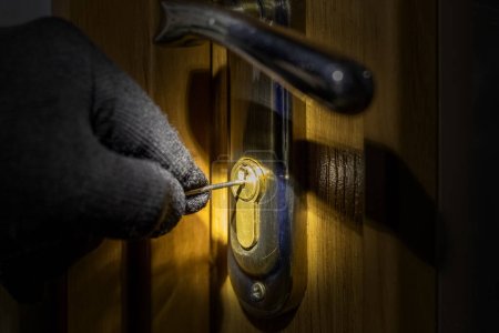 Téléchargez les photos : Le voleur essaie d'ouvrir la serrure de la porte avec une clé spéciale - en image libre de droit