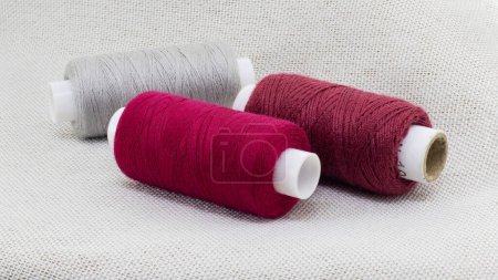 Photo for Spools of red, burgundy and gray threads lie on the fabric - Royalty Free Image