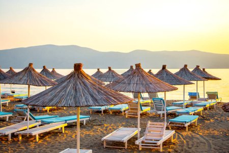 Straw umbrellas and sunbeds on the beach against the background of the sea in the morning