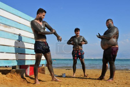 Foto de MUERTO MAR - NOV 10 2022: Grupo de hombres israelíes cubriéndose con un barro del Mar Muerto. El barro ayuda a restaurar la humedad y aliviar los síntomas, calmando la piel seca, áspera, irritada, acné, eczema y psoriasis. - Imagen libre de derechos