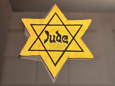 Foto de CANBERRA - MAR 14 2023: Parche judío estrella amarilla. Es una insignia de tela que a los judíos se les ordenó coser sus prendas exteriores para marcarse en público en ciertos momentos de su historia.. - Imagen libre de derechos