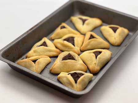 Purim jewish holiday cookies backed Hamentashen Ozen Haman in baking oven tray close up food background.