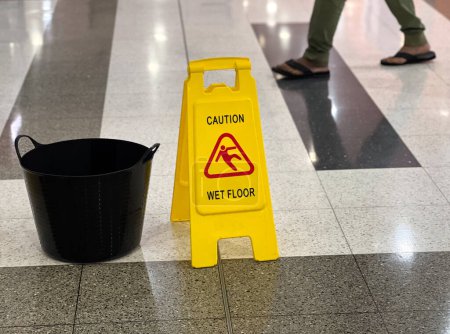 Photo for Unrecognizable person passing by a caution wet floor sign and a bucket - Royalty Free Image