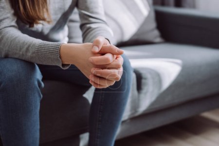 Photo for Unrecognizable female folded hands on knees together, sitting on couch alone, upset depressed girl feeling lonely, suffering from domestic violence or relationship problem, break up with boyfriend - Royalty Free Image
