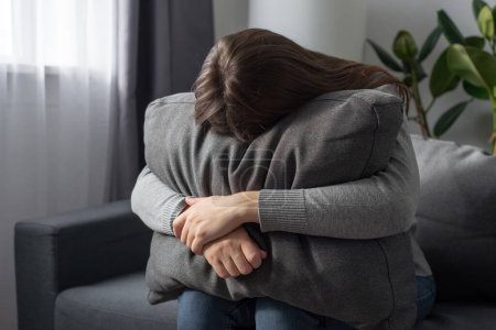 Mujer joven soltera deprimida sosteniendo almohada pasando por una crisis emocional después de abusar del aborto sentado en el sofá en casa sola. Mujer solitaria estresada en el sofá se esconden de los problemas del duro mundo cruel