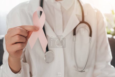 Foto de Primer plano de la doctora sosteniendo una pequeña cinta rosa para apoyar a las personas que viven y enferman. Salud, Día Internacional de la Mujer y concepto del Día Mundial del Cáncer. Octubre Mes de concientización sobre el cáncer de mama - Imagen libre de derechos