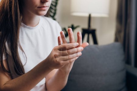 Kranke junge Frau mit Arthritis und Gelenkschmerzen in den Fingern, die zu Hause auf dem Sofa sitzt. Nahaufnahme der weiblichen Hand mit Symptomen chronischer Gicht. Gesundheitswesen einfache Selbstmassage-Konzept. Schmerzen in den Fingern