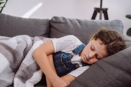 Photo for Close up of sick unhealthy preteen girl lying alone on sofa under blanket in living room at home. Ill upset caucasian child has fever. Concept of health, illness, sickness, common cold, treatment - Royalty Free Image