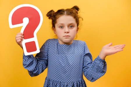 Photo for Portrait of pensive little girl kid 7-8 old years holding red question mark sign, confusion concept, posing isolated over plain yellow color background wall in studio. Childhood lifestyle concept - Royalty Free Image