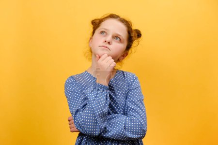 Photo for Portrait of thoughtful preteen girl kid contemplating about idea, touching her chin, posing isolated over plain yellow color background wall in studio. Hmm, let's think. Pensive and brainstorm concept - Royalty Free Image