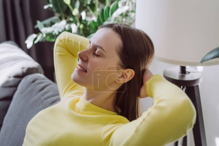 Close up of calm young woman resting breathing fresh air feeling mental balance enjoying wellbeing at home on couch, satisfied girl taking pleasure of stress free weekend morning stretching on couch