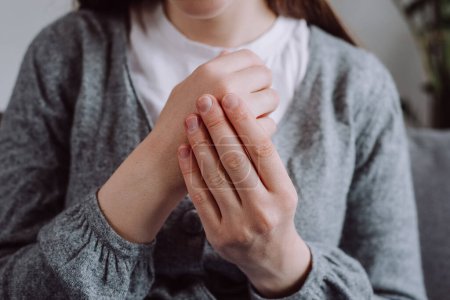 Close-up of female hand with symptoms of chronic gout. Health care easy self-massage concept. Pain in fingers. Sick young woman with arthritis and joint pain in fingers sitting on couch at home