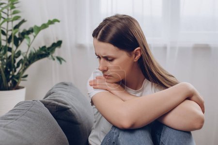 Frustrated confused woman feels unhappy, problems in personal life, quarrel break up with boyfriend and unexpected pregnancy concept. Anxious worried young female sitting alone on couch at home