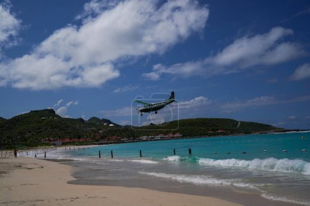 Photo for ST. BARTS, FRENCH WEST INDIES - APRIL 18, 2024: St Barth Commuter Cessna 208B Grand Caravan plane descends for landing at Remy de Haenen Airport also known as Saint Barthelemy Airport. At 2,133 ft its runway is one of the shortest in the world. - Royalty Free Image