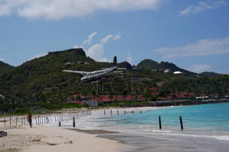 Photo for ST. BARTS, FRENCH WEST INDIES - APRIL 18, 2024: St Barth Commuter Cessna 208B Grand Caravan plane descends for landing at Remy de Haenen Airport also known as Saint Barthelemy Airport. At 2,133 ft its runway is one of the shortest in the world. - Royalty Free Image