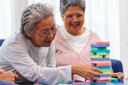 Photo for Senior people playing a wooden block tower, risk and strategy of project management. Concept of business risk with domino blocks. Older People playing jenga block removal game on table at home - Royalty Free Image