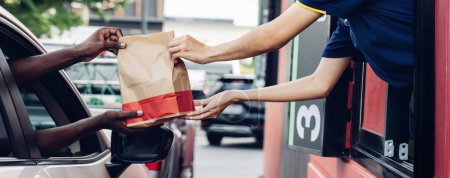 Hand Mann im Auto empfängt Kaffee in Fahrt durch Fast-Food-Restaurant. Personal bedient Imbissbestellung für Fahrer im Lieferfenster. Durchfahren und Mitnehmen für Fast Food kaufen zum Schutz von Covid19.