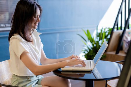 Woman working on laptop computer sitting at home and managing her business via home office during Coronavirus or Covid-19 quarantine. woman using laptop and smiling while working at Home