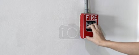 Téléchargez les photos : Woamn ou travailleur poussant l'alarme incendie sur le mur. Un feu ! ou Cas d'urgence au bâtiment de l'usine. Équipement d'alarme ou d'alerte incendie ou d'alarme cloche - en image libre de droit