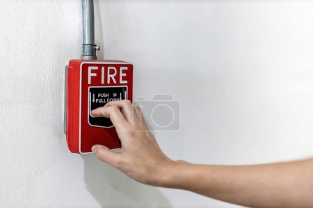 Woamn oder Arbeiter drücken Brandmelder an die Wand. Ein Feuer! oder Notfall im Fabrikgebäude. Notfall von Brandmelde- oder Alarm- oder Klingelwarngeräten