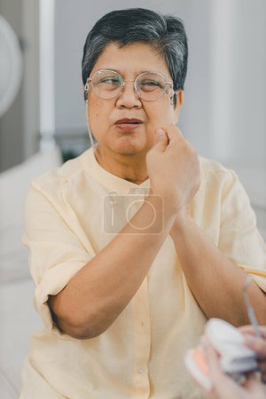 Seniorin mit Zahnschmerzen. Frau hat Zahnschmerzen, berührt ihre Zähne und runzelt vor Schmerzen die Stirn. Zahnschmerzen und Zahnheilkunde