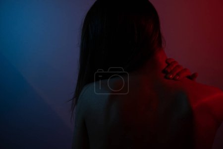 Photo for Intense young woman, blue and red lighting on back. Neck and back pain.Mental burden concept - Royalty Free Image