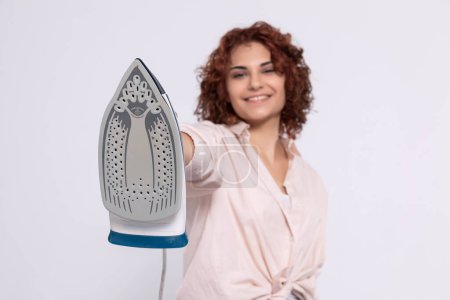Foto de A girl with short and curly hair. An adult coquette holds an iron in her hand. Total readiness to iron clothes. - Imagen libre de derechos