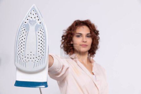 Téléchargez les photos : A girl with short and curly hair. An adult coquette holds an iron in her hand. Total readiness to iron clothes. - en image libre de droit