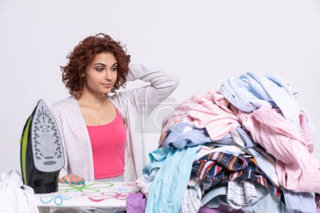 Foto de A woman wonders how to get down to ironing such a large amount of clothing. The surprised look on the girls face before starting her homework. - Imagen libre de derechos