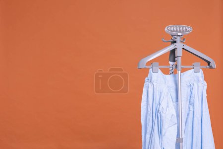 Photo for Mens shirt. Hot steam device for ironing clothes with hanger. Uniform brick-colored background. Isolated from the background. - Royalty Free Image
