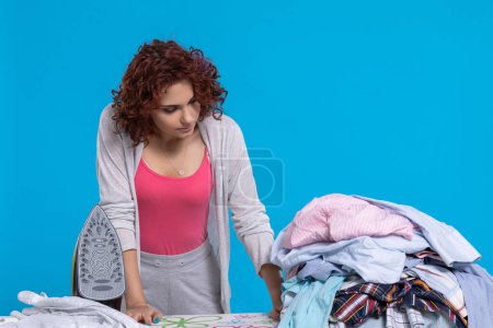 Photo for Not too thrilled, the housewife, that so many shirts to iron. Ironing board with crumpled shirts and iron ready to go. - Royalty Free Image