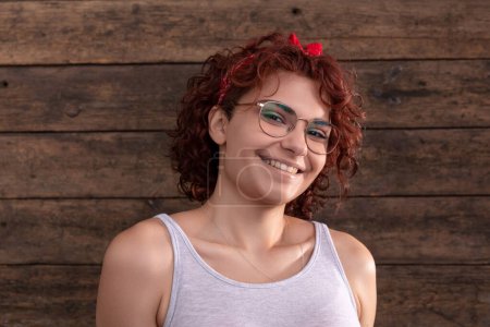 Téléchargez les photos : European woman with a sincere smile and short curly hair. A wall of brown-colored boards. Dressed in a gray sports T-shirt. - en image libre de droit