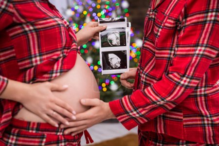Photo for In the foreground, the torso of a woman and a man facing each other. The woman is advanced in pregnancy and exposes her belly. The couple jointly hold an usg photo of the baby, visible in the - Royalty Free Image