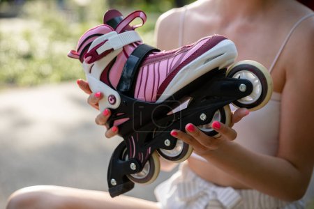 Photo for Large close-up on rollerblade in shades of purple and gray. Blurred background. In the background a figure of a girl holding a rollerblade in her hands. A woman with short pink nails sitting on a - Royalty Free Image