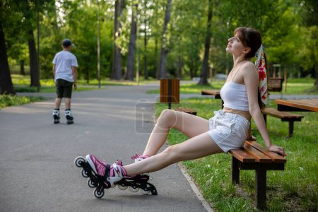 Photo for Roller skating in a city park. Active spending time on a summer sunny day. Person dressed in summer sportswear in shades of white. In the background the distant figure of a boy riding on roller skates - Royalty Free Image