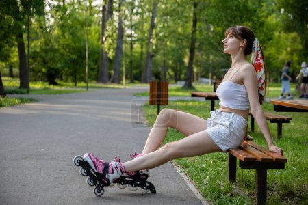 Skater-Mädchen entspannt sich nach dem Training. Rollschuhlaufen im Stadtpark. Aktive Zeit an einem sonnigen Sommertag. Person in sommerlicher Sportbekleidung in Weißtönen.