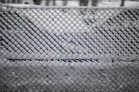 Foto de Snow se ha instalado en una cerca de alambre. Primer plano de una cerca congelada cubierta de nieve. Los espacios entre el alambre están llenos de nieve y hielo. - Imagen libre de derechos