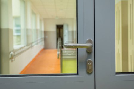 Salas de pasillo divididas por una puerta de aluminio con cristal. Vista de una sección de la puerta con una manija de color berlina.