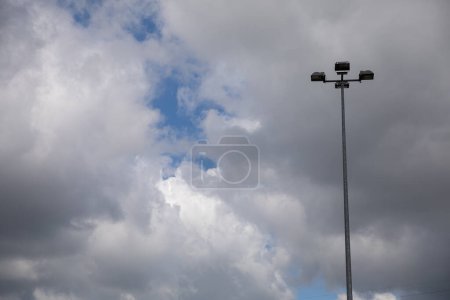 Foto de Led lámpara cuádruple en un poste alto contra un cielo con nubes blancas. Vista diurna del alumbrado público moderno. - Imagen libre de derechos