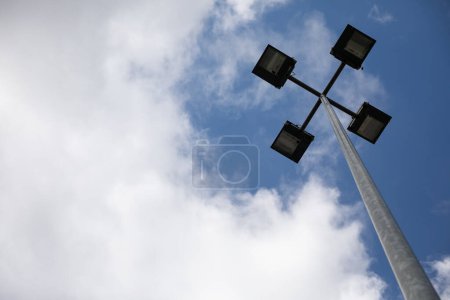 Foto de Una vista lejana de una linterna de luz de calle contra un cielo nublado. Lámpara cuádruple led en un poste redondo alto. - Imagen libre de derechos