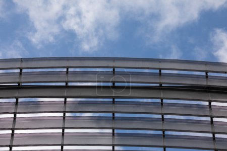 Téléchargez les photos : Une vue sur le sommet de la salle de sport contre un ciel bleu obscurci par des nuages blancs. Façade moderne du bâtiment en panneaux métalliques. - en image libre de droit